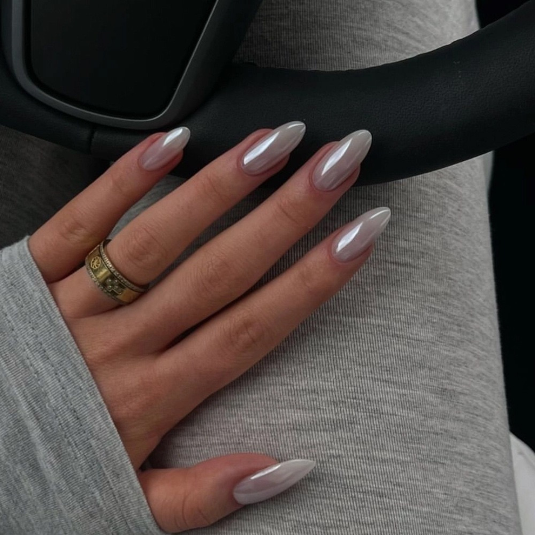 Close-up of a hand with long, pointed nails wearing a gold ring on a dark background