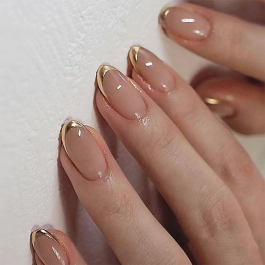 Close-up of a hand with beige nail polish and gold tips on a light background